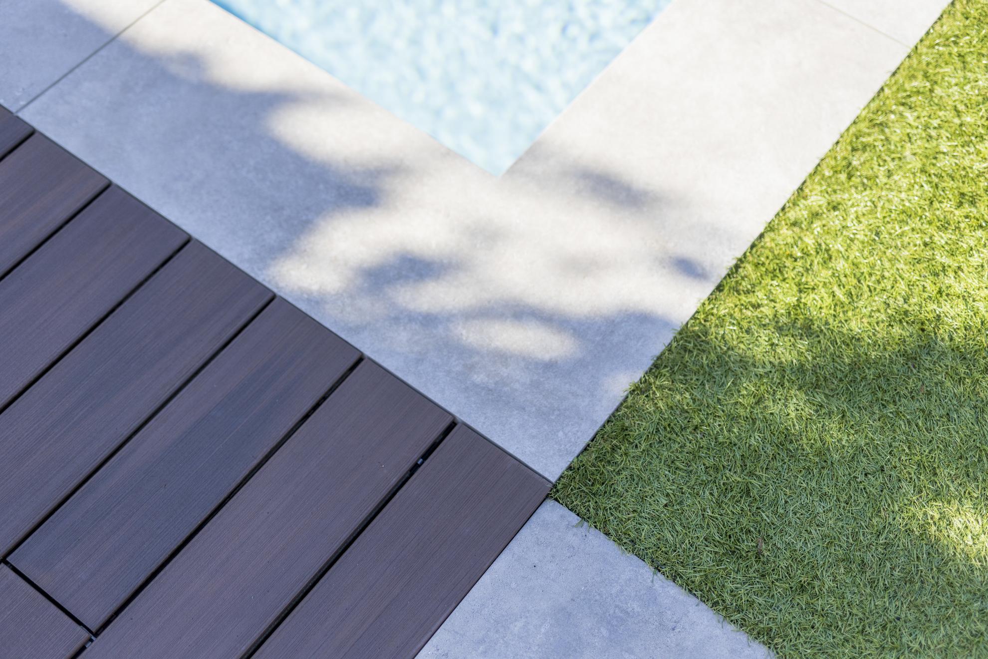 Margelle en pierre claire bordant une piscine, créant une transition élégante avec la terrasse en bois composite Silvadec foncé et la pelouse pour un aménagement extérieur harmonieux
