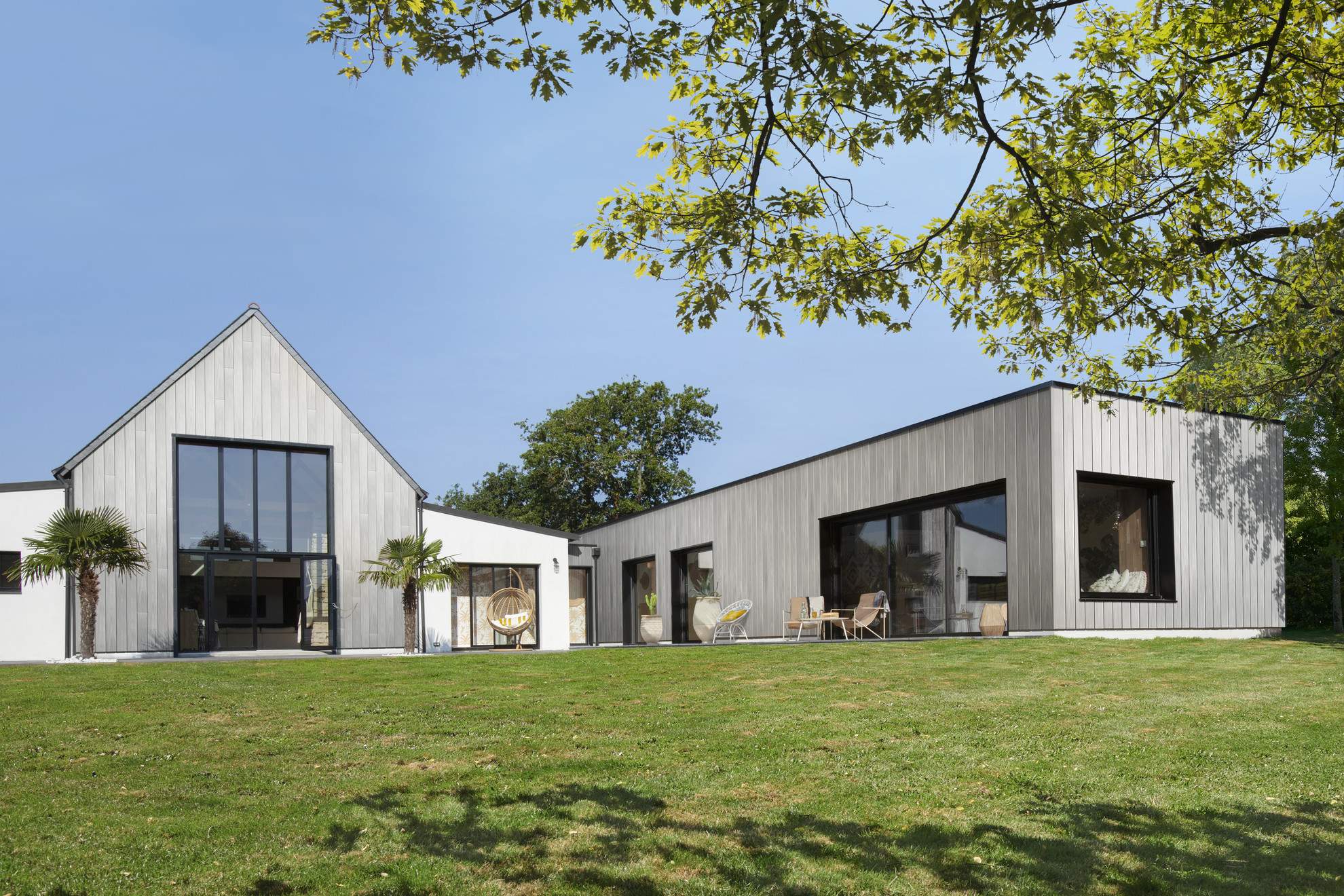 Contemporary house with Silvadec composite wood cladding, composed of two distinct volumes with pitched and flat roofs, surrounded by a lush garden