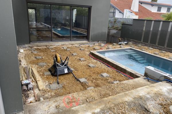 Terrain terrassé et préparé avec sable stabilisé autour d'une piscine, première étape avant l'installation d'une terrasse en bois composite, avec maison contemporaine et baies vitrées visibles à gauche
