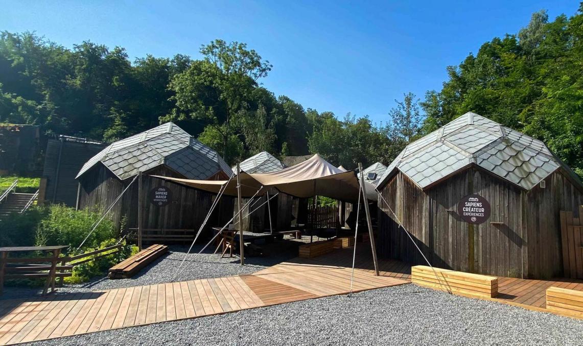 Wooden exhibition cabins with composite PRM ramp, slate roofs and shade sails, set in a landscaped area with gravel and vegetation